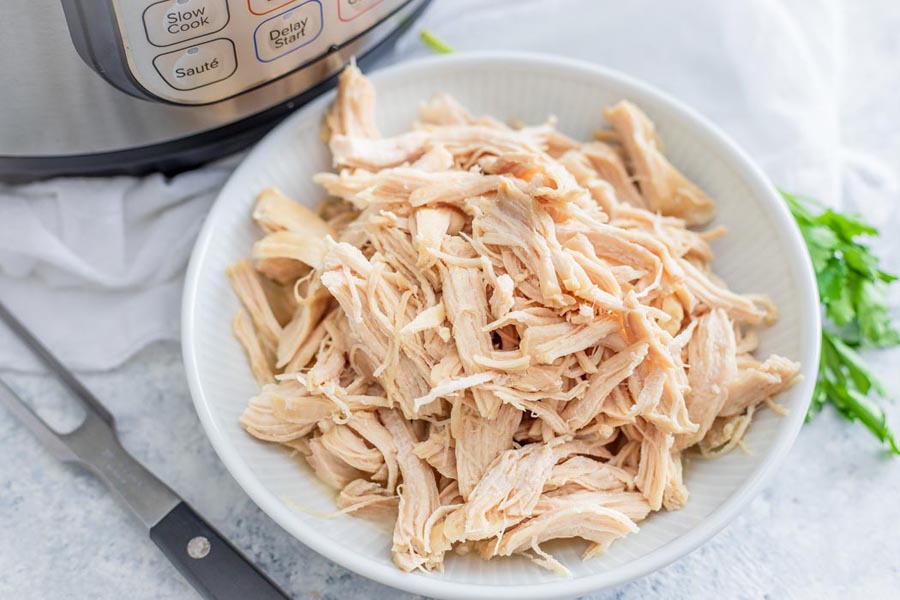 shredded chicken in a white bowl next to an instant pot