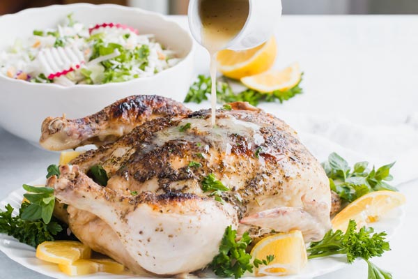 pouring lemon herb gravy on a roasted chicken