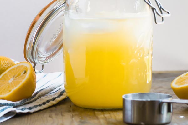 a pitcher filled with lemonade with squeezed lemons around it