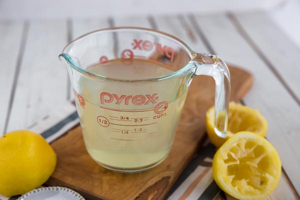 a glass of concentrated lemon juice on a cutting board with lemons