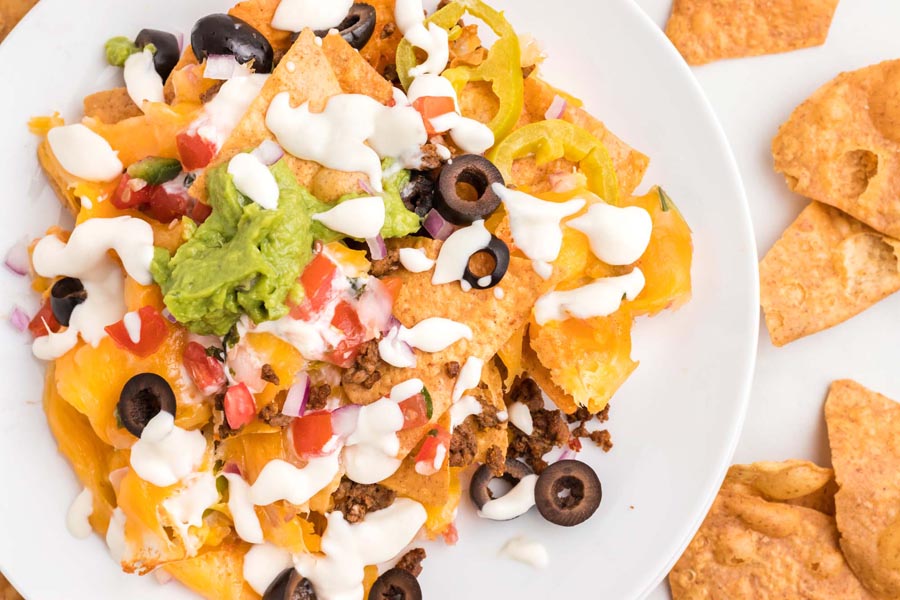 Looking down on a plate of beef nachos topped the a cream sauce, pico, red onion, olives and guacamole.