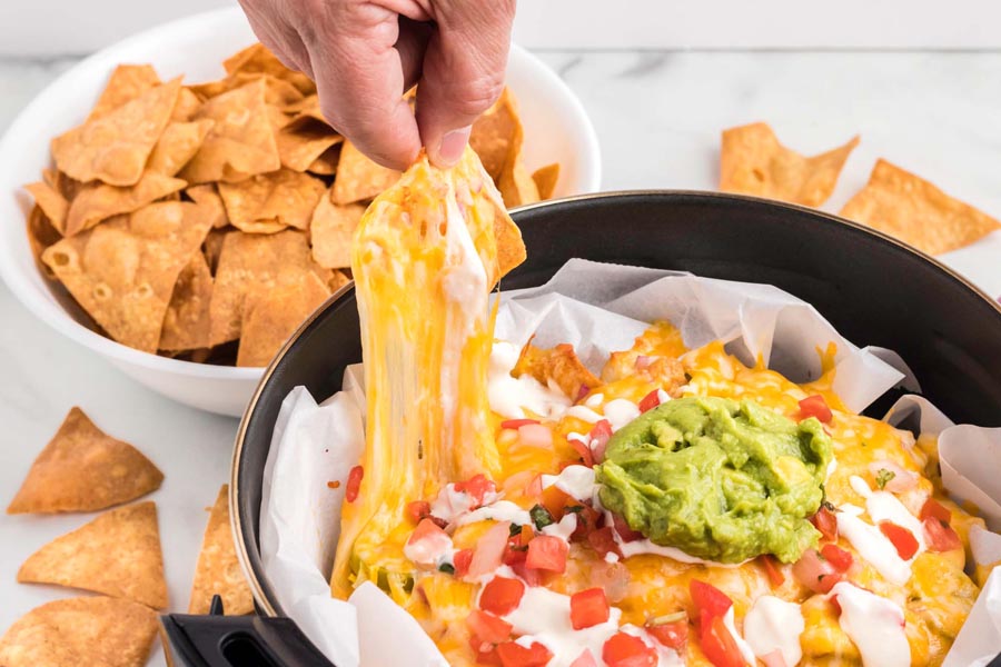 A hand pulling a chip covered in cheese while the cheese pulls away.