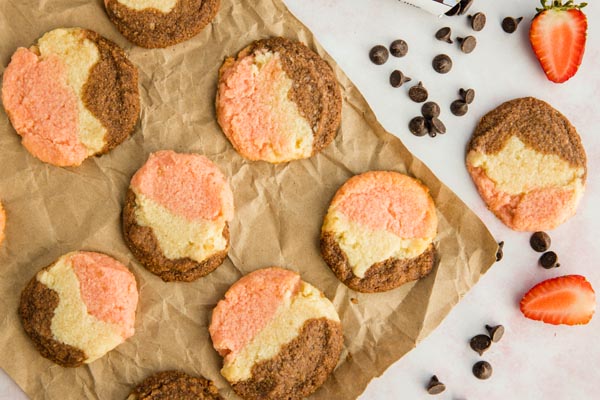 a bunch of neapolitan cookies on a brown paper with strawberries and chocolate chips nearby