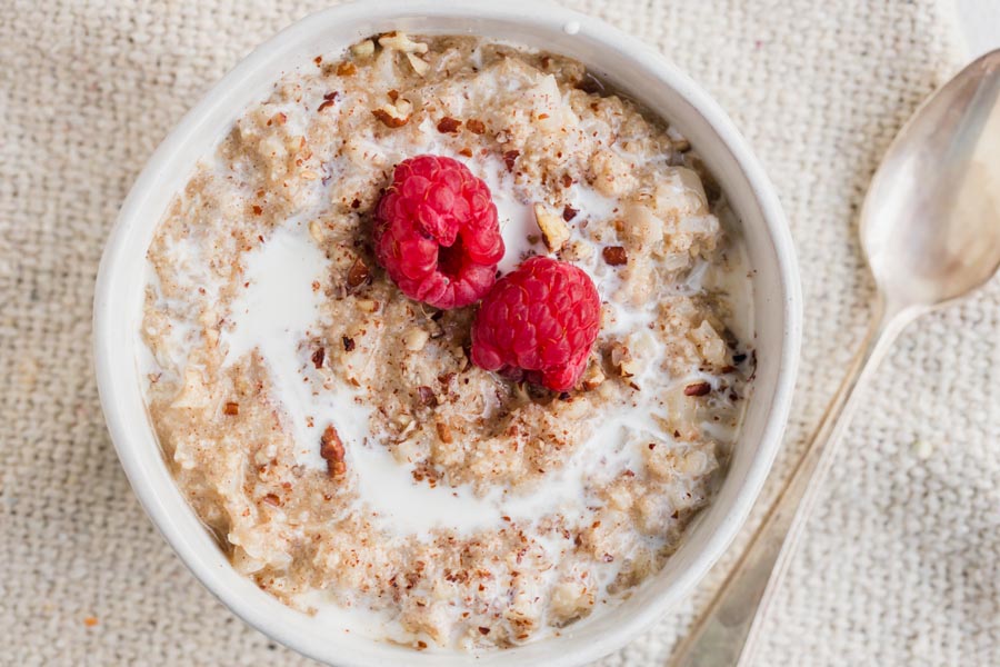 A small bowl of oatmeal topped with raspberries, chopped nuts and cream.