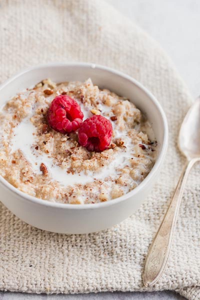 A bowl of oatmeal on a burlap cloth with a spoon next to it. The oatmeal is topped with berries.