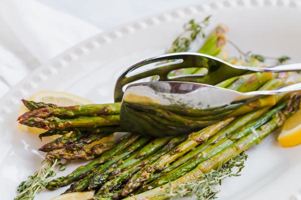 crispy roasted asparagus on a white platter with tongs