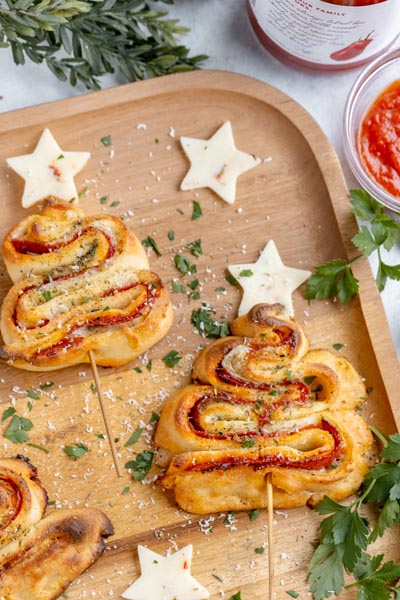 Christmas tree appetizer skewers on a wooden board with cheese stars around and parsley.