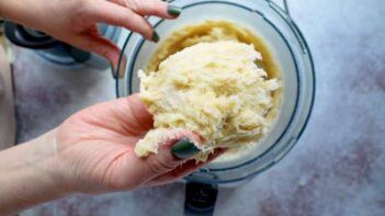 A hand holding fathead dough over a food processor.