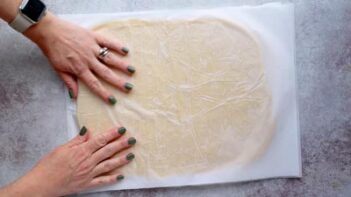 Keto pastry dough rolled out into a rectangle shape with a sheet of parchment paper on top.