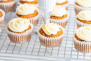 piping cream cheese frosting on a pumpkin muffin