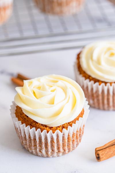 Two frosted cupcakes next to each other with a cinnamon stick nearby.