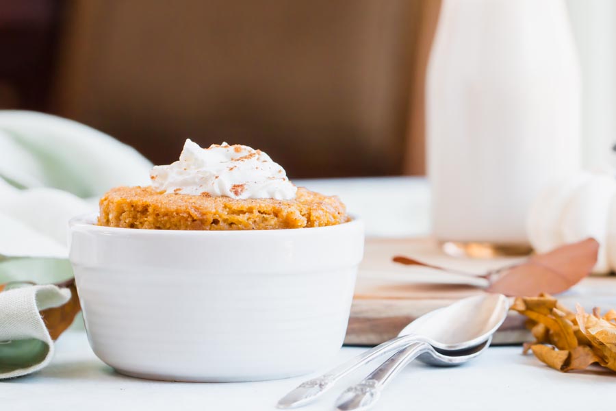 straight on view of an orange cake coming out of a white bowl with two spoons and milk in the background