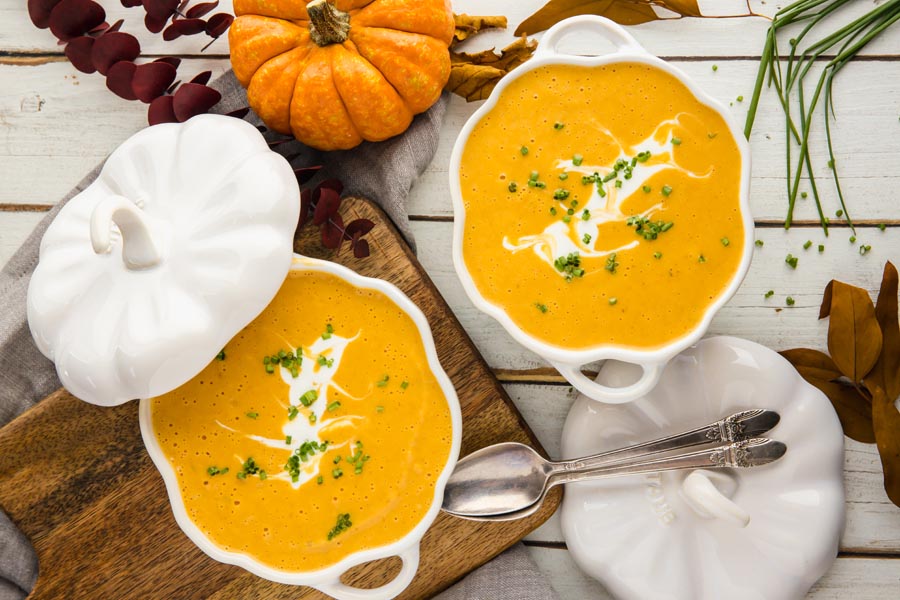 overhead view of keto soup in white pumpkin bowls with spoons and an orange pumpkine