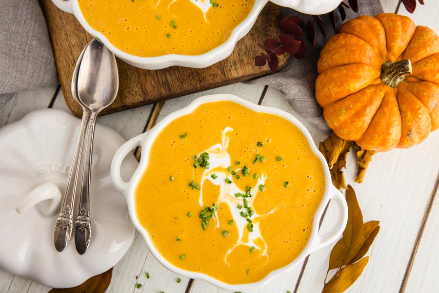 a bowl of pumpkin soup with two spoons pointing to another bowl of soup