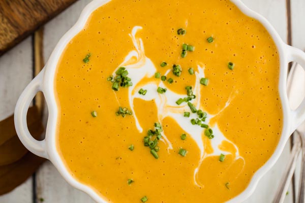 sour cream streaked on top of pumpkin soup and chives sprinkled around