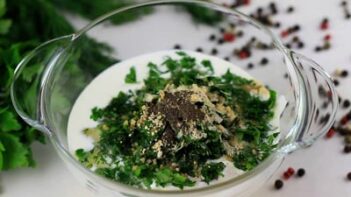 ingredients for ranch dressing in a clear bowl with peppercorns scattered around