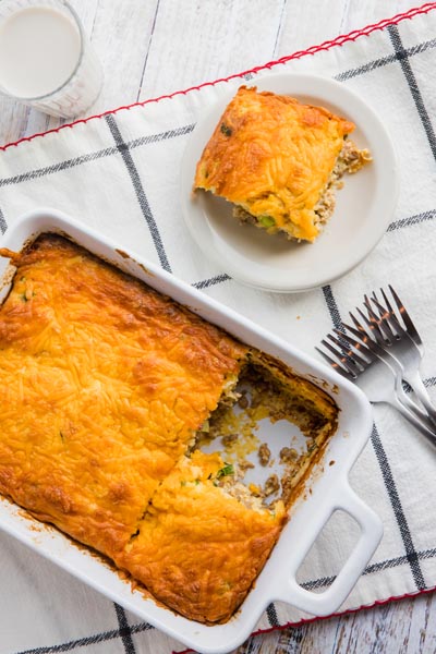 A cheese covered casserole in a white dish with forks nearby and a slice on a plate.