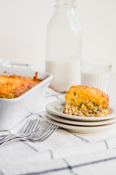 A slice of breakfast egg casserole on a stack of plates in front of milk.