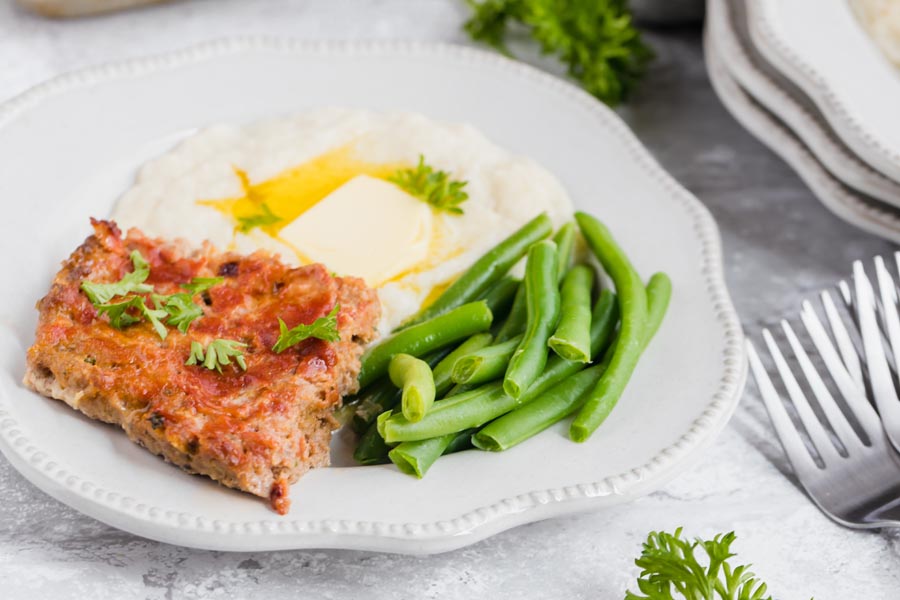 plate with keto meatloaf covered in ketchup with a side of beans and mashed cauliflower