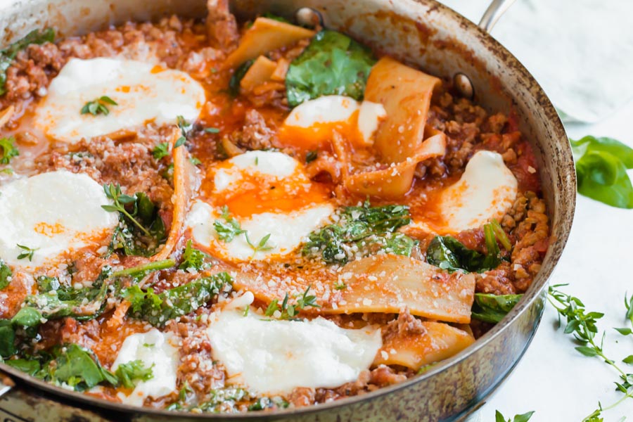 beef and tomato lasagna in a skillet with sheets of hearts of palm noodles and slices of mozzarella cheese