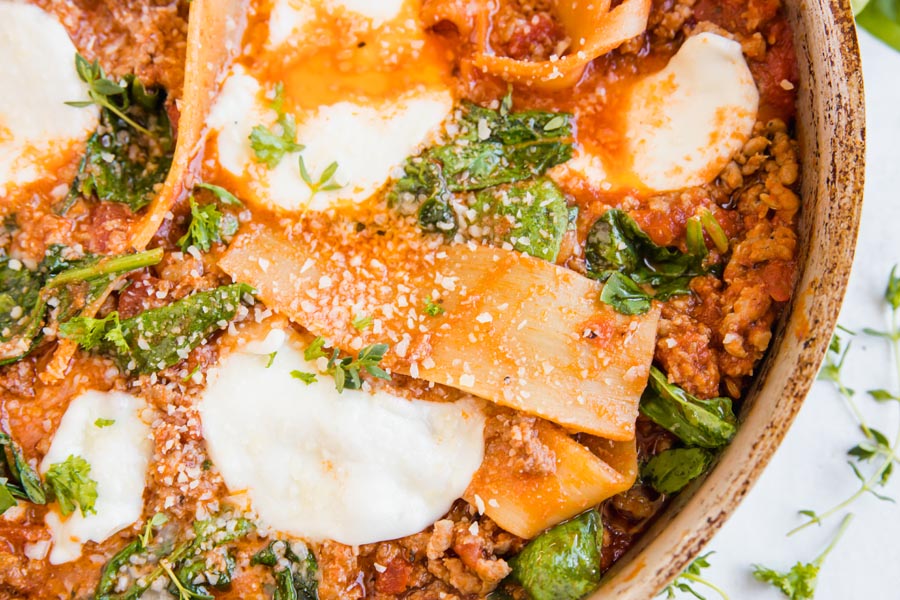 close up overhead view of cheesy beefy keto lasagna in a skillet topped with spinach