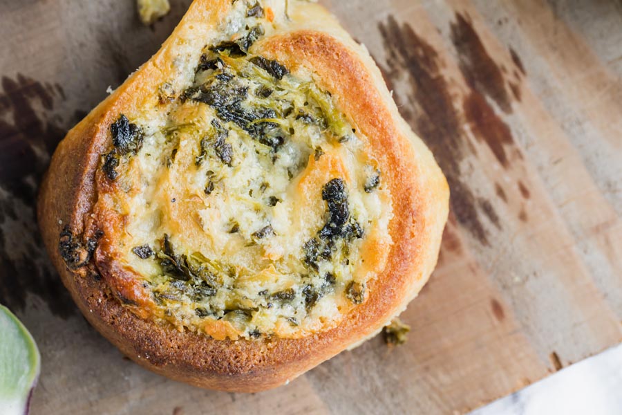 Close up of a cheesy, spinach pinwheel roll on a wooden board.