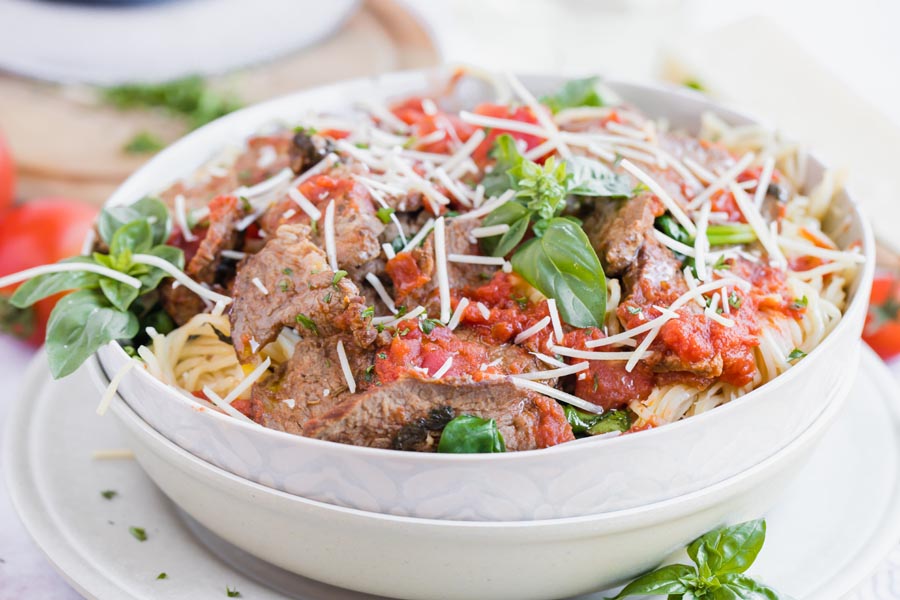 steak marinara dinner in a bowl with basil leaves top and a glass of wine in the background