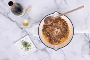 Cooked mushroom stems in a skillet next to a wine bottle and minced thyme.