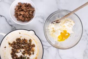 A bowl with cream cheese, egg yolk and parmesan cheese next to cooked sausage and mushrooms.