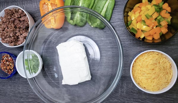 a bowl with cream cheese surrounded by bell peppers and ground beef