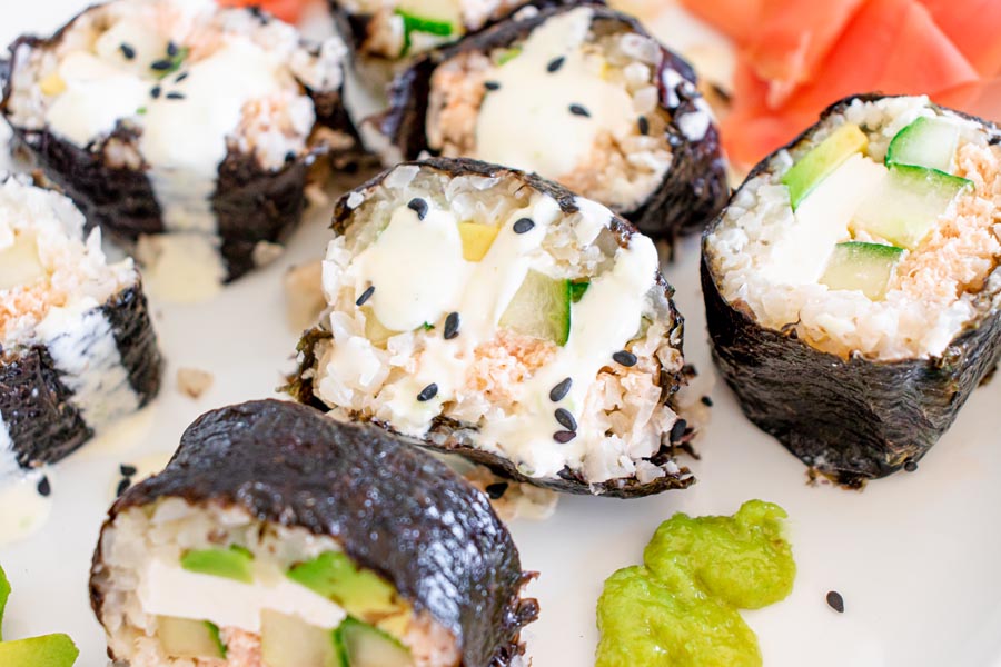 Close up of wasabi cream drizzled over sushi rolls and topped with black sesame seeds.