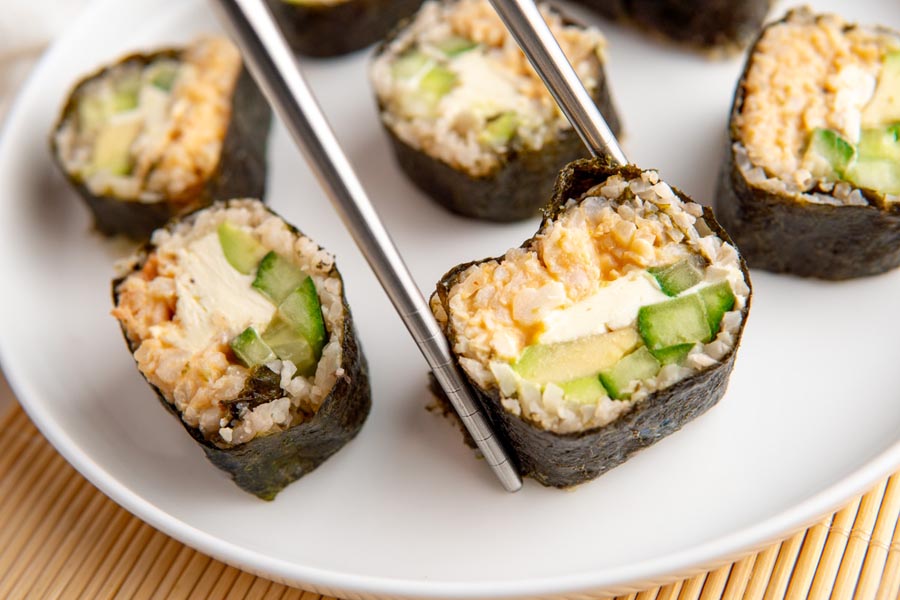 Metal chopsticks holding a california roll filled with crab, cucumber and avocado.