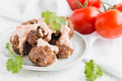 keto taco meatballs next to tomatoes on a plate topped with sauce