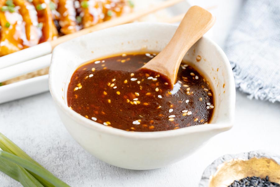 a wooden spoon sitting in a beige bowl with brown sauce in it