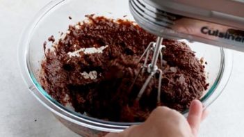 pouring a chocolate mixture into a bowl with dry ingredients