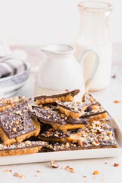 A dish filled with broken pieces of toffee with a creamer and milk behind.