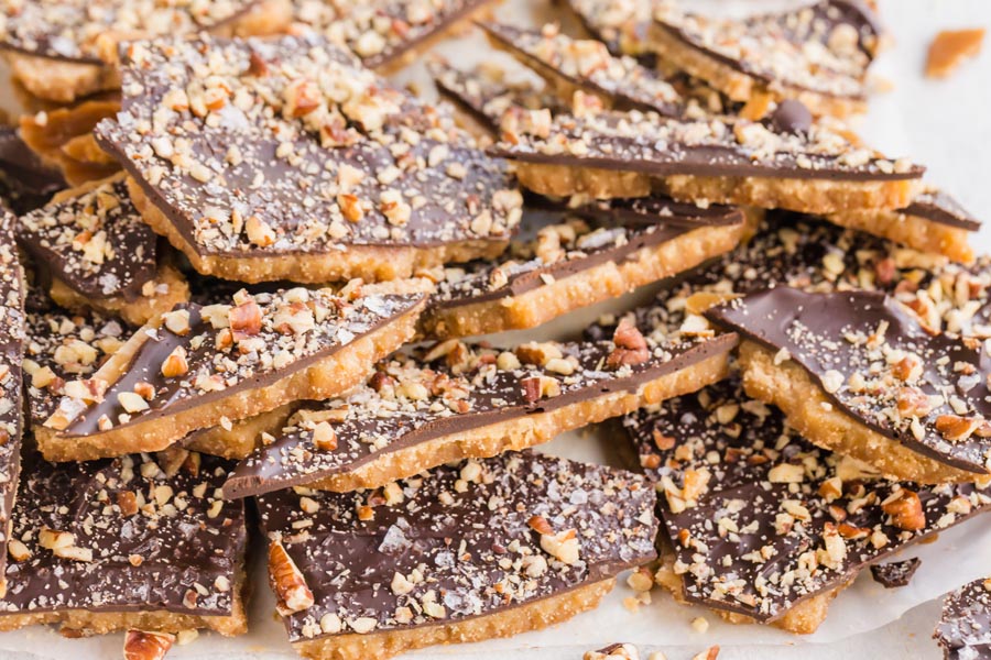 Candied toffee in a pile topped with chocolate and nuts.