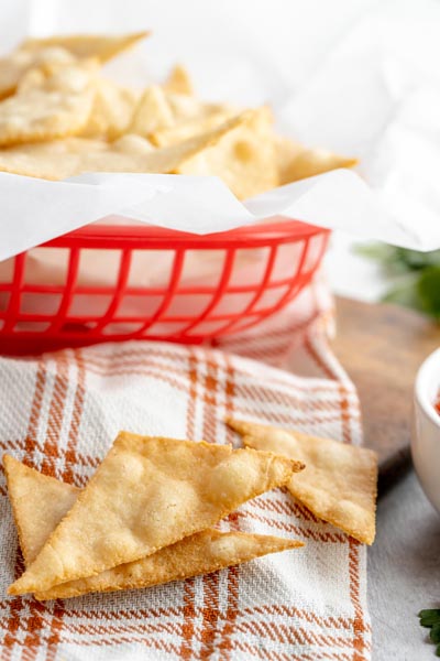 three corn tortilla chips on a cream and orange colored towel in front of a red basket of more chips