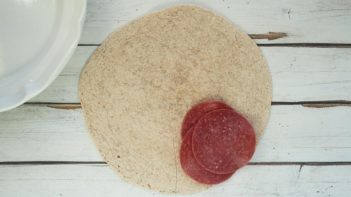 three slices of salami on top of a tortilla in one corner