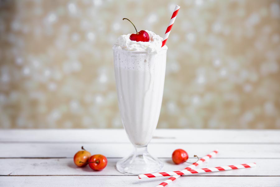 creamy vanilla shake in a traditional milkshake glass topped with whipped cream and a red swirly straw