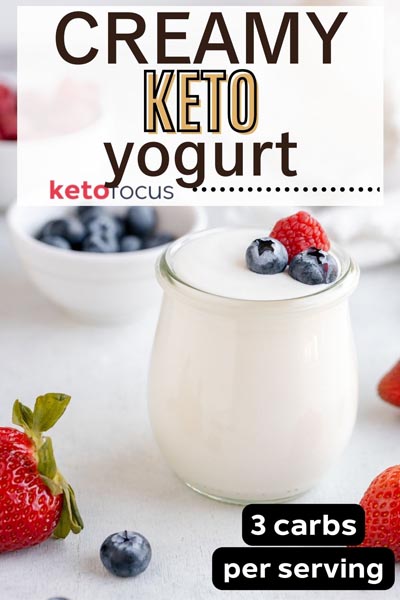 Creamy keto yogurt in a jar topped with berries and berries scattered around.