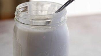 A mason jar with yogurt and a spoon sticking out.