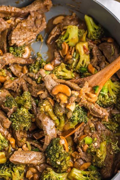 A wooden spoon holding a serving of saucy cashew beef with broccoli.