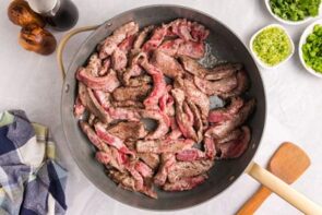 Strips of flank steak searing in a skillet.