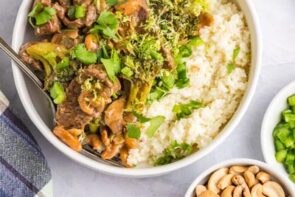 A bowl with cashew beef next to cauliflower rice and topped with cilantro.