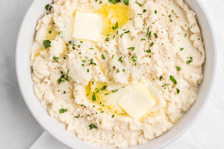 Two pats of butter melting over a bowl of mashed turnips.