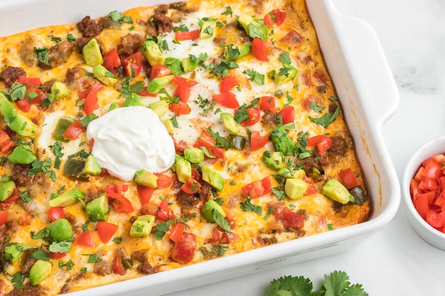 Colorful casserole topped with avocado, sour cream, tomato and cilantro.