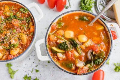 a spoon in a small bowl of tomato based minestrone soup