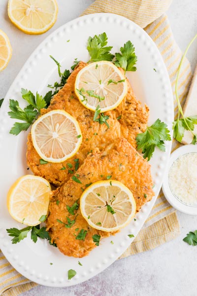 a dinner plate with two fried chicken cutlets on them next to grated parmesan cheese and lemon slices