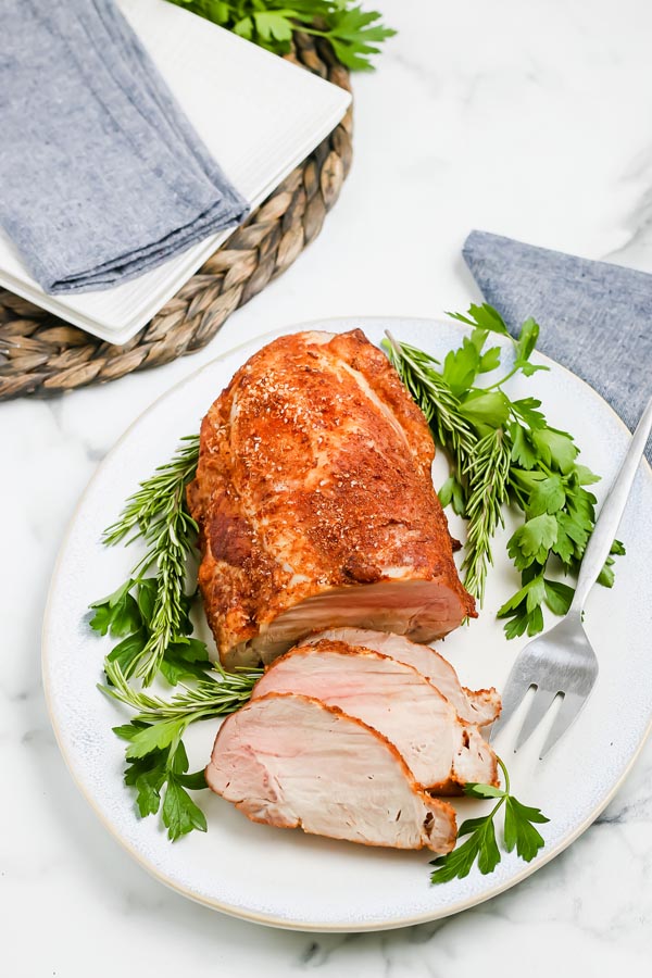 a whole pork roast on a white platter with slices of roast on the plate too and a fork